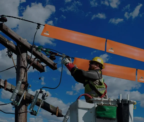 A Importância do teste de EPI com tensão aplicada nos equipamentos de segurança e ferramentais isolantes. Descrição da imagem: Um técnico realizando uma manutenção em uma rede elétrica energizada de 13800 V. O técnico utiliza os equipamentos de proteção individual como luva isolante, a luva de cobertura que fica sobre a luva de borracha para realizar a proteção mecânica da luva de borracha, também o profissional utiliza capacete isolante e os seguintes equipamentos de proteção coletivo, manta isolante que é colocado sobre os fios para que o profissional possa aproximar da linha energizada em levar choque e também uma cesto aéreo que faz a suspensão do profissional para realizar o trabalho em altura.A Lumens Calibração situado em Guarulhos, São Paulo. Realizamos atendimento em todo Brasil.