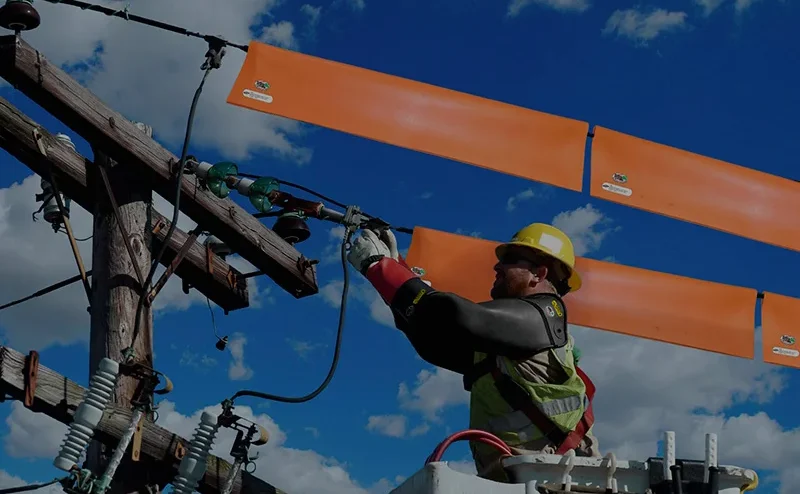 A Importância do teste de EPI com tensão aplicada nos equipamentos de segurança e ferramentais isolantes. Descrição da imagem: Um técnico realizando uma manutenção em uma rede elétrica energizada de 13800 V. O técnico utiliza os equipamentos de proteção individual como luva isolante, a luva de cobertura que fica sobre a luva de borracha para realizar a proteção mecânica da luva de borracha, também o profissional utiliza capacete isolante e os seguintes equipamentos de proteção coletivo, manta isolante que é colocado sobre os fios para que o profissional possa aproximar da linha energizada em levar choque e também uma cesto aéreo que faz a suspensão do profissional para realizar o trabalho em altura.A Lumens Calibração situado em Guarulhos, São Paulo. Realizamos atendimento em todo Brasil.